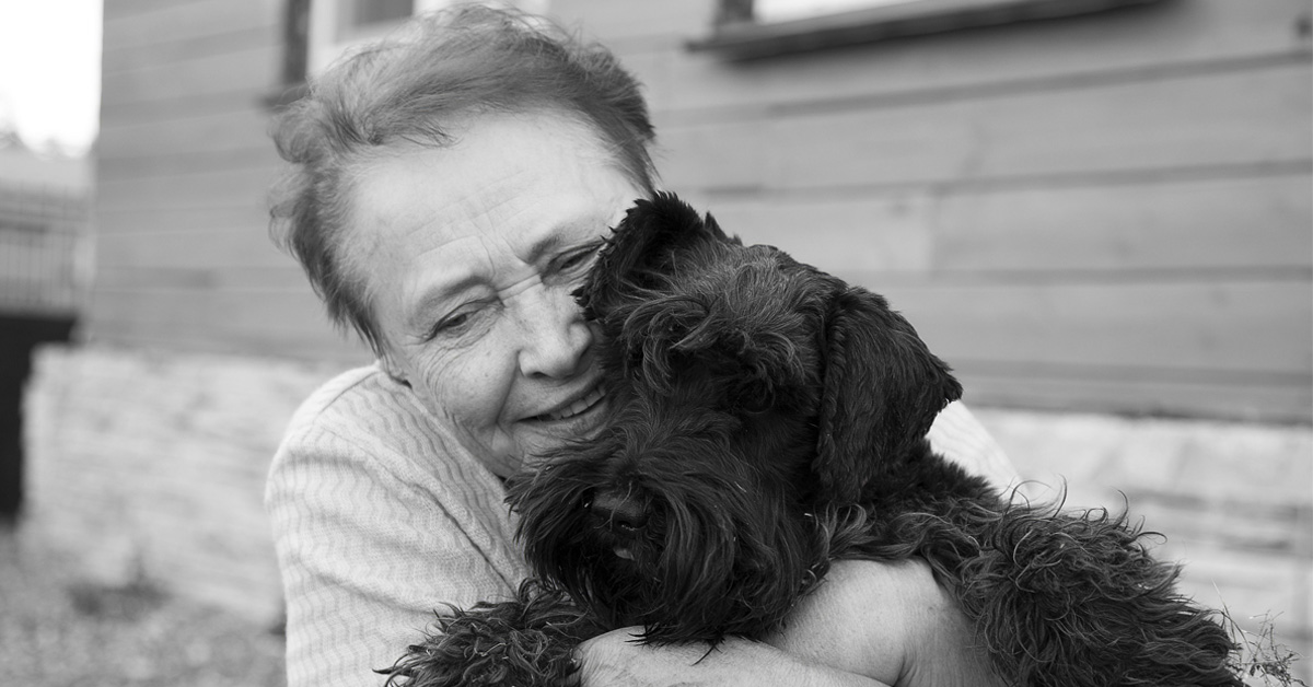 Pet Ownership and Effect on Mental Health in Seniors. Black & White picture of an elderly caucasian female hugging a little black dog.