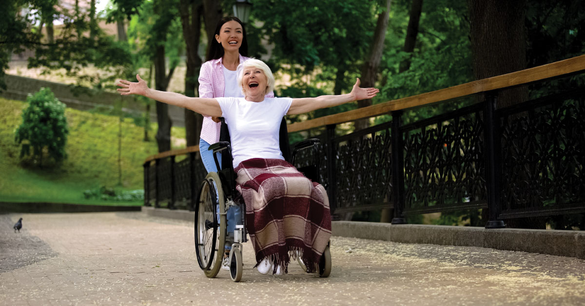 Don’t Let Limited Mobility Stop You From Being Active . Picture of a young asian female pushing an older caucasian female in a wheelchair.